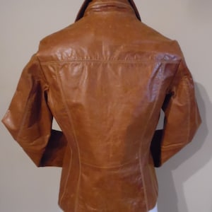 May include: A brown leather jacket with a collared neckline and long sleeves. The jacket has a fitted silhouette and a smooth leather finish.