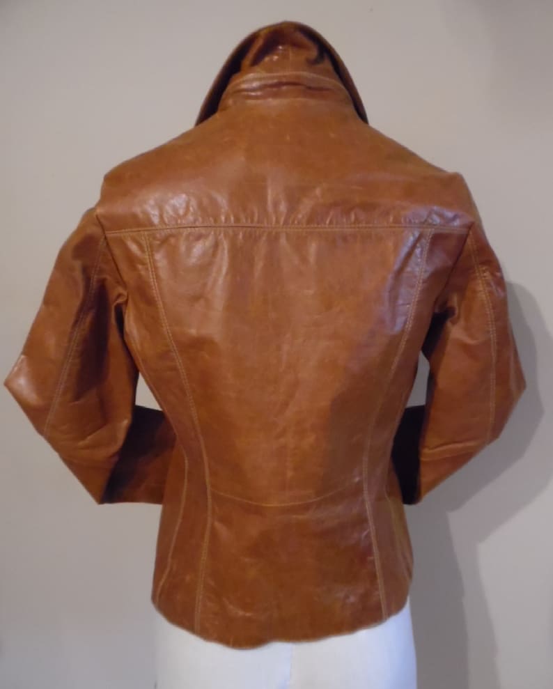 May include: A brown leather jacket with a collared neckline and long sleeves. The jacket has a fitted silhouette and a smooth leather finish.