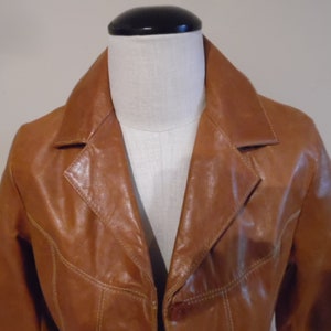 May include: A brown leather jacket with a button closure and a collar. The jacket has a slightly distressed look and is made of a soft, supple leather.