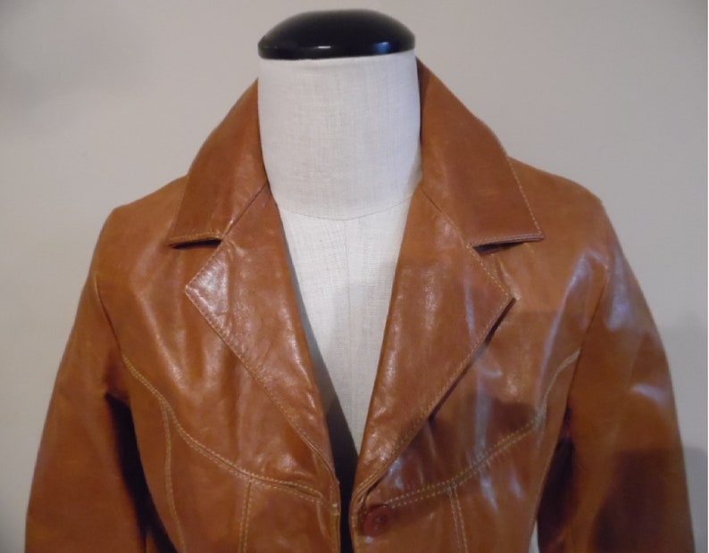 May include: A brown leather jacket with a button closure and a collar. The jacket has a slightly distressed look and is made of a soft, supple leather.