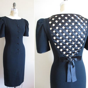 May include: A black dress with a fitted silhouette and short puff sleeves. The back of the dress features a unique design with a black and white lattice pattern.