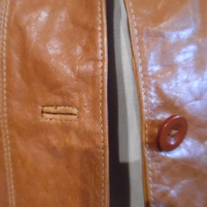 May include: Close-up of a brown leather jacket with a button and stitching detail.