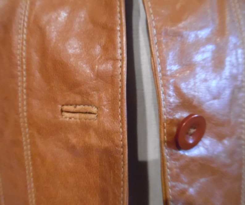 May include: Close-up of a brown leather jacket with a button and stitching detail.