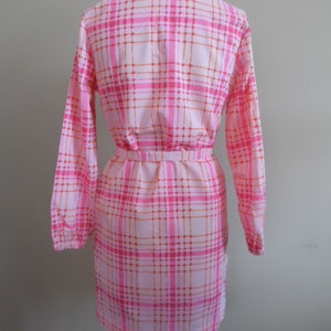 May include: A pink and orange plaid dress with long sleeves and a belt. The dress has a collared neckline and a button-up front.