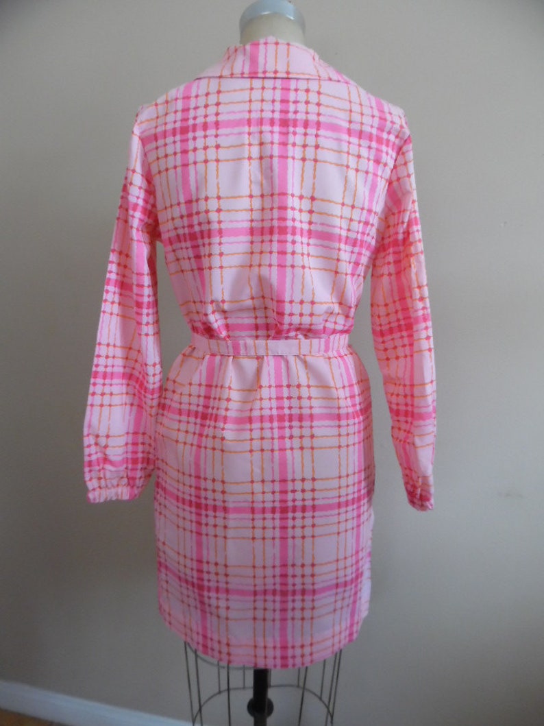 May include: A pink and orange plaid dress with long sleeves and a belt. The dress has a collared neckline and a button-up front.