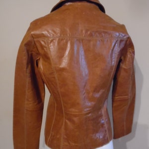 May include: A brown leather jacket with a collared neckline and long sleeves. The jacket has a fitted silhouette and a smooth leather finish.