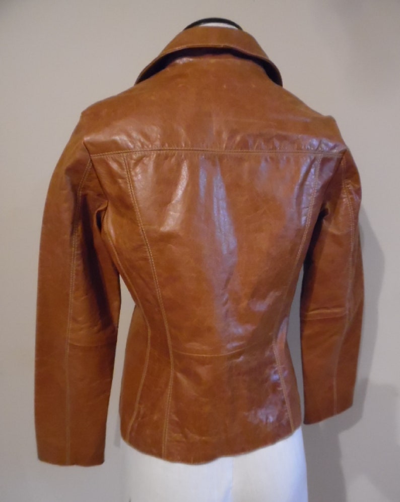 May include: A brown leather jacket with a collared neckline and long sleeves. The jacket has a fitted silhouette and a smooth leather finish.