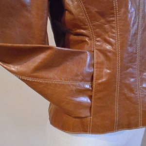 May include: A brown leather jacket with a button closure and a seam detail. The jacket has a pocket on the left side.