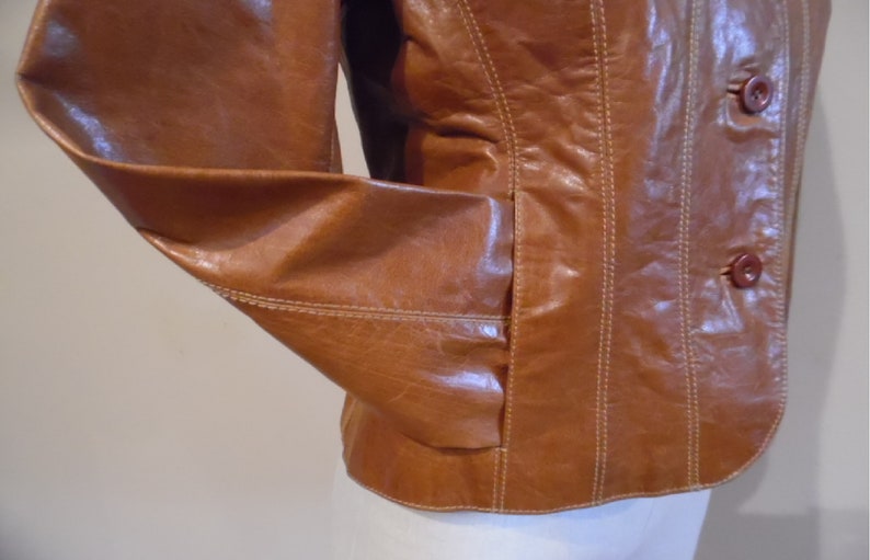 May include: A brown leather jacket with a button closure and a seam detail. The jacket has a pocket on the left side.