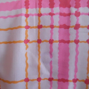 May include: A white fabric with a pink and orange plaid pattern. The fabric has a soft, woven texture.
