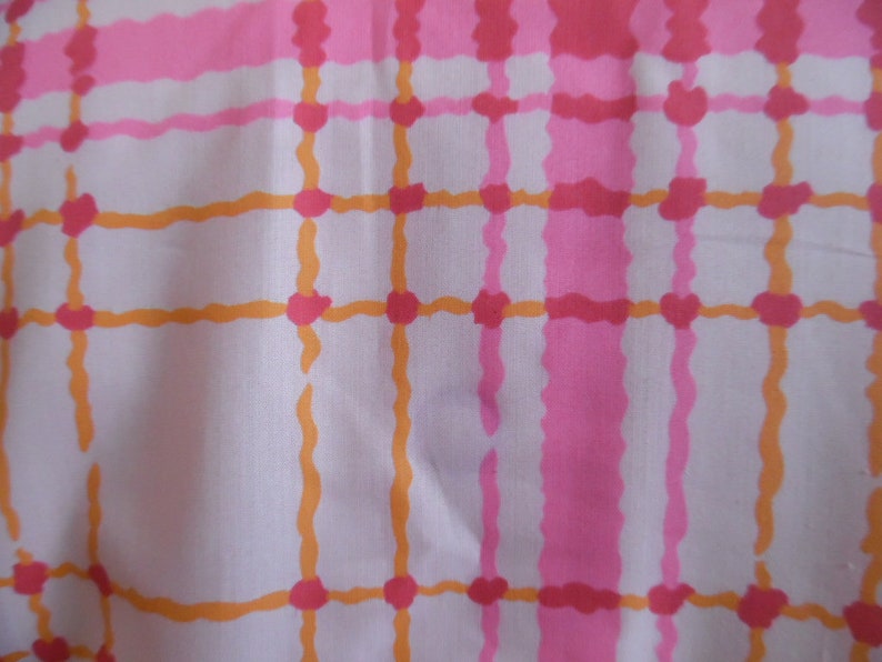 May include: A white fabric with a pink and orange plaid pattern. The fabric has a soft, woven texture.