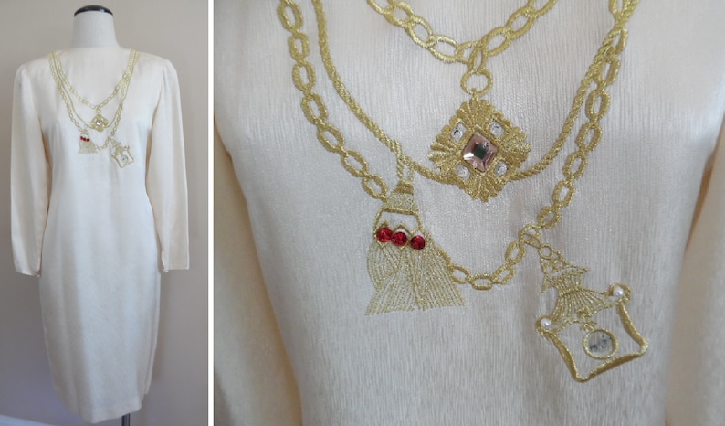 Pode incluir: Vestido creme de manga comprida com design de colar bordado a ouro. O colar apresenta um pingente em forma de diamante com uma gema rosa, uma borla com detalhes vermelhos e um pingente de frasco de perfume com uma gema transparente.