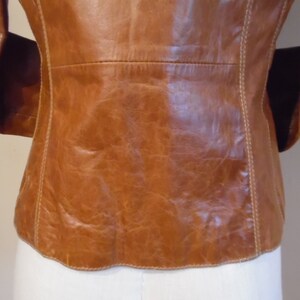 May include: A brown leather jacket with a white stitch detail around the edges. The jacket is unbuttoned and the back is visible.