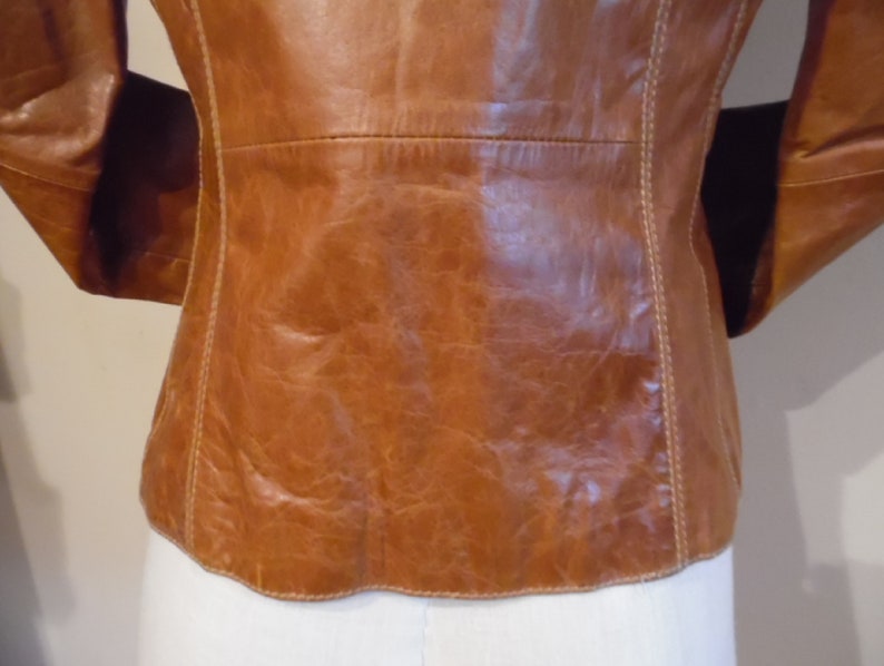 May include: A brown leather jacket with a white stitch detail around the edges. The jacket is unbuttoned and the back is visible.
