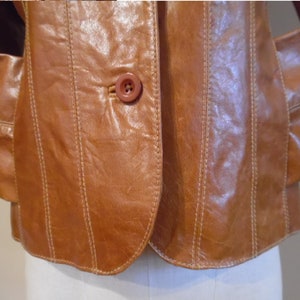 May include: A brown leather jacket with a single button closure and vertical stitching details.