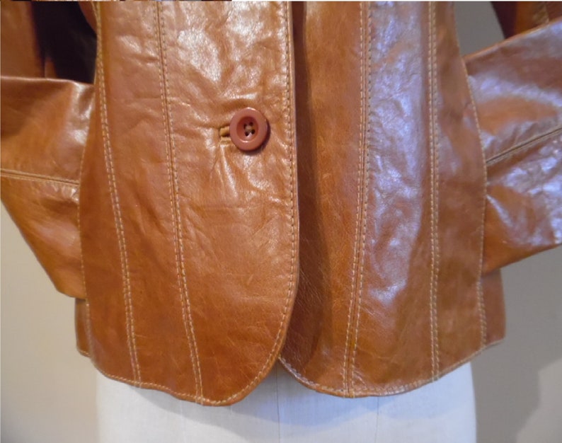 May include: A brown leather jacket with a single button closure and vertical stitching details.