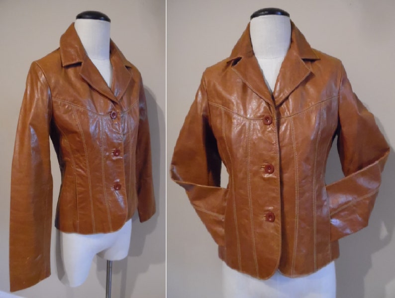 May include: A brown leather jacket with a button-up front and a collar. The jacket has a fitted silhouette and is lined with a brown fabric.