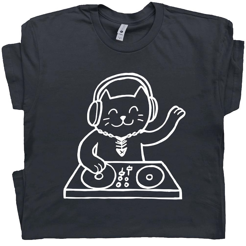 May include: Dark gray t-shirt featuring a white cartoon cat DJ wearing headphones and a necklace. The cat is smiling and has one paw raised. The cat is standing behind a DJ mixing board.