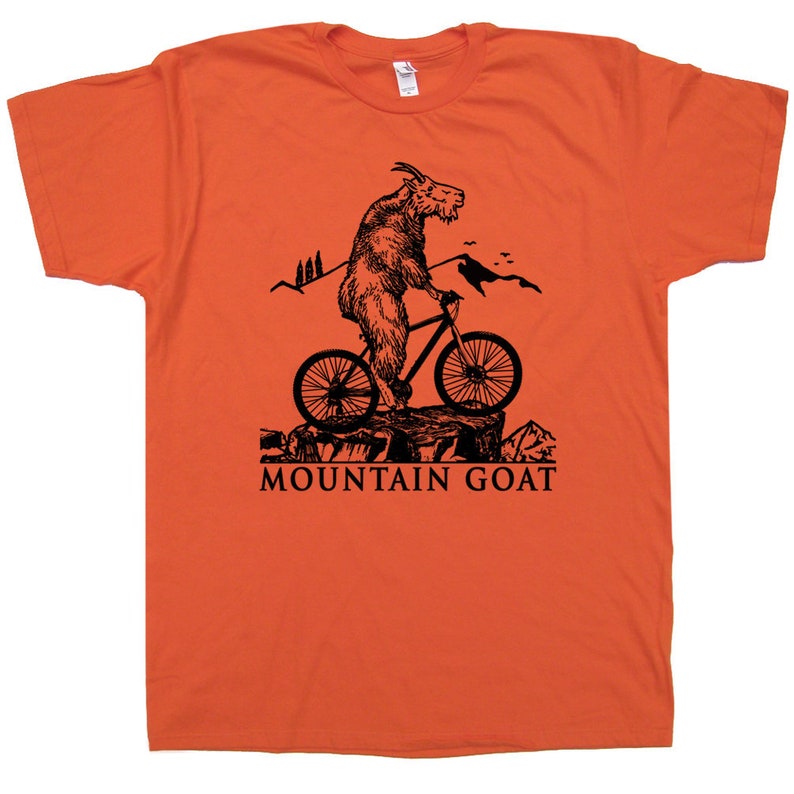 May include: Orange t-shirt with a black graphic of a mountain goat riding a bicycle. The text "MOUNTAIN GOAT" is printed below the image.