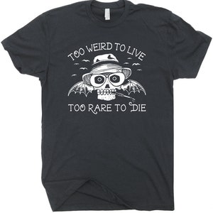 May include: Black t-shirt with a white skull wearing a hat and sunglasses. The skull has bat wings and is holding a cigarette. The text "Too Weird To Live Too Rare To Die" is printed on the shirt.