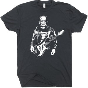 May include: Dark gray t-shirt featuring a white graphic of Frankenstein playing a bass guitar. The design includes a leather jacket and a shirt that says "METAL". The bass guitar has a lightning bolt design.