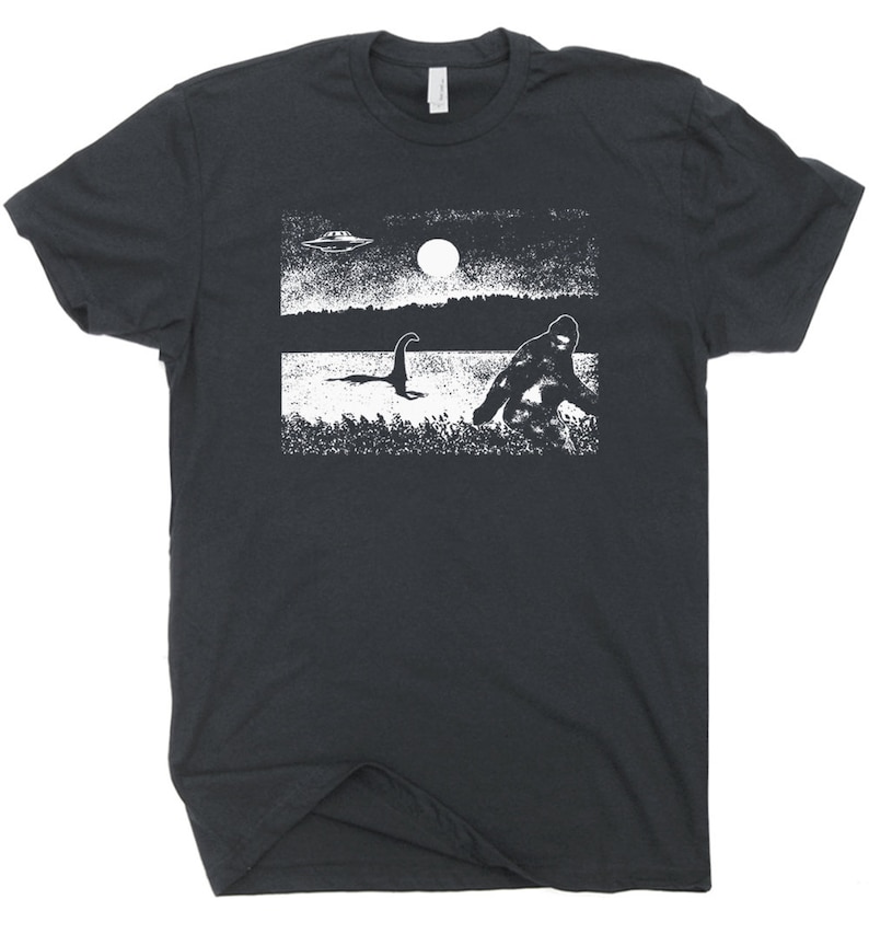 Puede incluir: Una camiseta negra con un estampado gr&aacute;fico blanco de un OVNI, Bigfoot y el monstruo del Lago Ness. El gr&aacute;fico est&aacute; en un estilo desgastado.