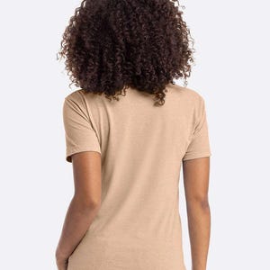 May include: A tan short-sleeve t-shirt. The shirt is made of a soft, heathered fabric. The model has dark curly hair.