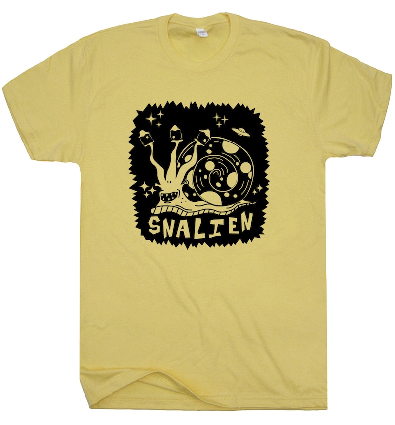 May include: A yellow t-shirt with a black graphic of a snail with a UFO and stars. The text "SNALIEN" is below the snail.