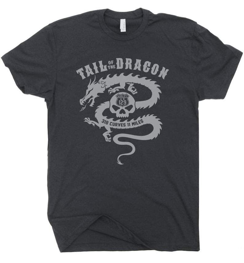 Może przedstawiać: Szary t-shirt z szarym nadrukiem przedstawiającym smoka z czaszką w paszczy. Tekst "Tail of the Dragon" znajduje się nad smokiem, a tekst "318 Curves 11 Miles" pod smokiem. Czaszka ma logo Harley Davidson i numer 129.
