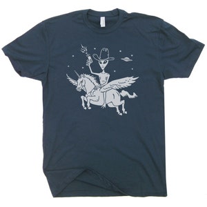 May include: A navy blue t-shirt with a white graphic of an alien wearing a cowboy hat and riding a winged unicorn. The alien is holding a gun and there are stars in the background.
