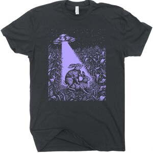 May include: A dark gray t-shirt with a purple graphic of two rabbits in a cornfield with a UFO hovering above them.