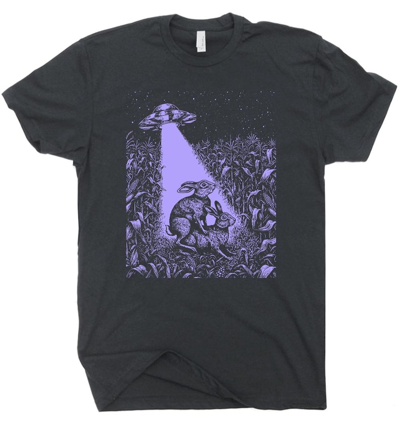 May include: A dark gray t-shirt with a purple graphic of two rabbits in a cornfield with a UFO hovering above them.