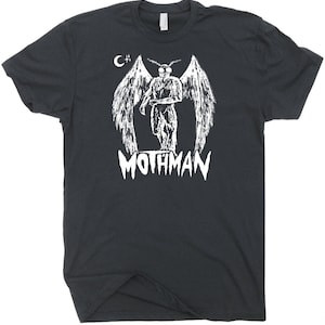 Peut inclure: T-shirt noir avec un motif blanc d'une cr&eacute;ature ail&eacute;e et le texte "Mothman" en dessous. Le motif comprend &eacute;galement une lune croissante et un signe plus.