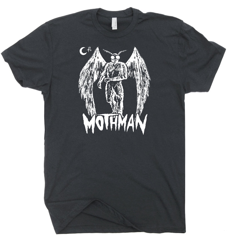 Peut inclure: T-shirt noir avec un motif blanc d'une cr&eacute;ature ail&eacute;e et le texte "Mothman" en dessous. Le motif comprend &eacute;galement une lune croissante et un signe plus.