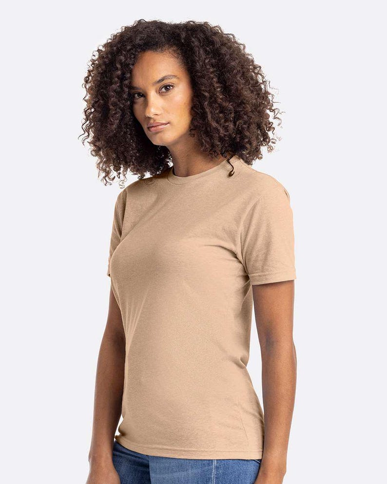 May include: A tan-colored, short-sleeved t-shirt. The shirt has a crew neck and a simple, classic design. The fabric appears to be a soft, heathered material. The model is wearing the shirt.