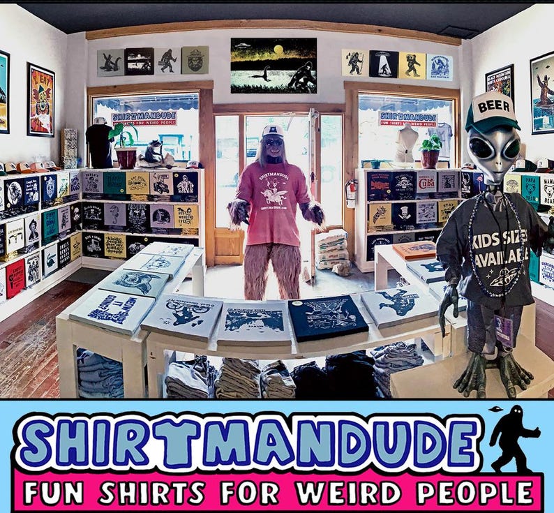 May include: A store called "Shirtmandu" with the tagline "Fun Shirts for Weird People". The store is decorated with a variety of shirts, including a shirt with a creature from the Black Lagoon, a shirt with a mushroom, and a shirt with a beer logo. There is also a large, furry, pink creature wearing a shirt with a cartoon image of a creature.