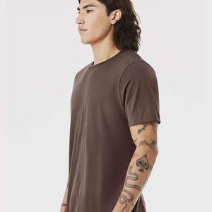 May include: A solid brown crew neck t-shirt. The short-sleeved shirt is made of a soft material. The model is wearing the shirt. The shirt is a basic wardrobe staple.