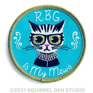 May include: Embroidered patch featuring a cat with glasses and a judicial collar, with the text "RBG is My Mews" on a teal background. The patch has a gold border and white embroidered details. A fun, cat-themed accessory.
