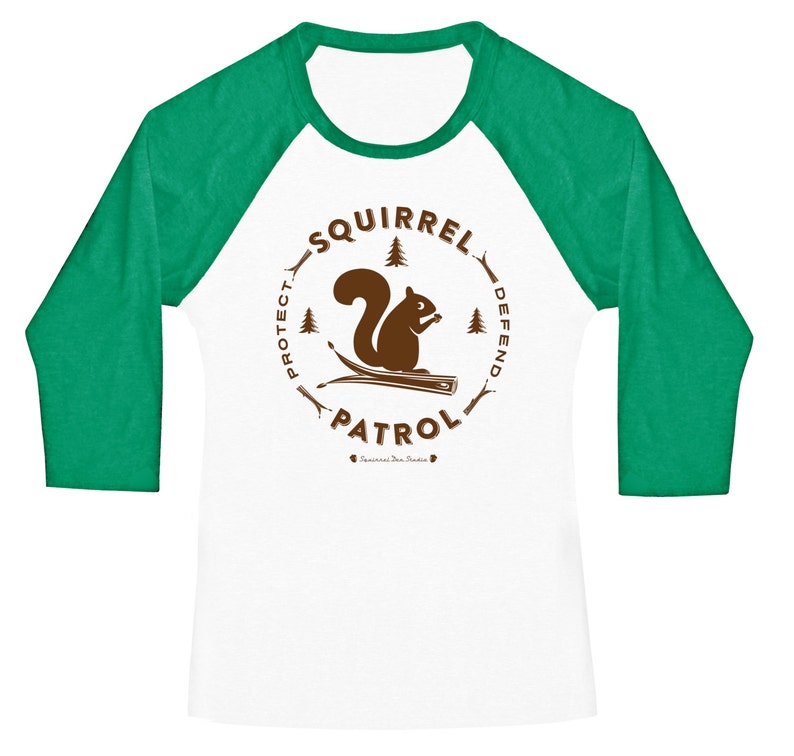 May include: A white and green baseball tee shirt with a brown graphic of a squirrel on a branch. The graphic is surrounded by a circle with the text "Squirrel Patrol" and the words "Protect" and "Defend" on either side of the squirrel.