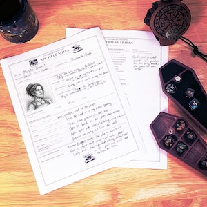 May include: A tabletop roleplaying game character sheet titled NPC FIELD NOTES with handwritten details about Magda Ironfist, a black leather dice bag with a circular embossed design, and two dark brown coffin-shaped dice trays containing polyhedral dice.