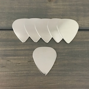May include: Seven silver guitar picks arranged in a row, with one silver guitar pick below the row.