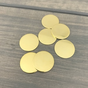 May include: A group of seven gold-colored metal circles, arranged in a loose cluster on a woodgrain surface.