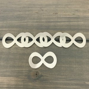 May include: A set of six silver infinity symbol charms, with one charm placed below the others. The charms are made of metal and have a shiny finish.