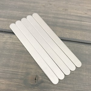 May include: Five silver metal strips, each with rounded ends, are stacked on top of each other on a gray wooden surface.