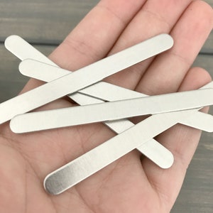 May include: Five silver metal nose wire pieces for face masks. The wires are straight and have rounded ends.