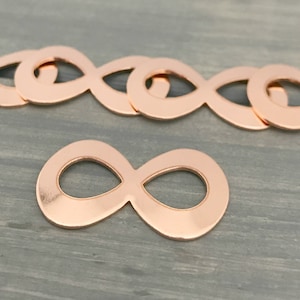 Puede incluir: Un grupo de ocho dijes de infinito de oro rosa, con un dije en primer plano. Los dijes son de metal y tienen un acabado brillante.
