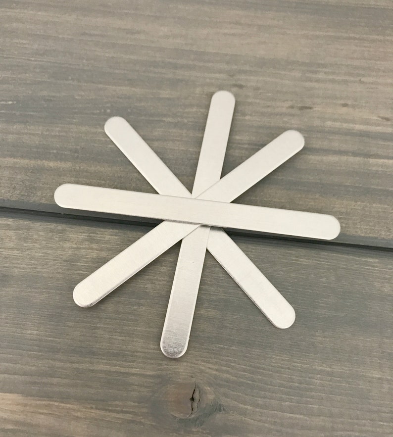 May include: A set of six silver metal craft sticks arranged in a star shape on a woodgrain surface.