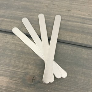 May include: Five silver metal craft sticks, arranged in a fan shape on a gray wooden surface.