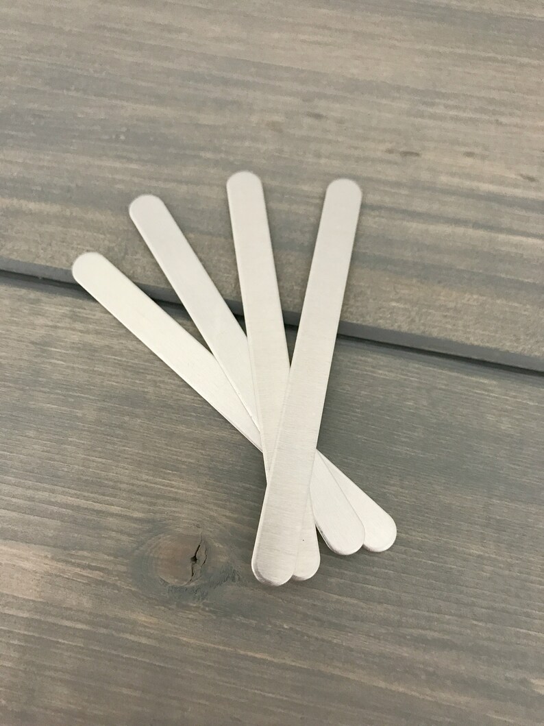 May include: Five silver metal craft sticks, arranged in a fan shape on a gray wooden surface.