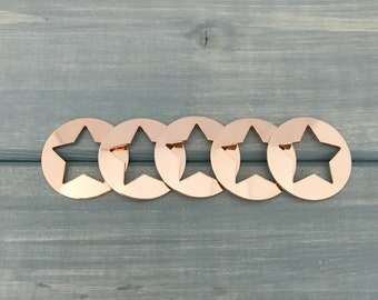 Könnte beinhalten: Fünf goldfarbene, sternförmige Kerzenringe aus Metall. Die Ringe sind in einer Reihe auf einer grauen Holzoberfläche angeordnet.